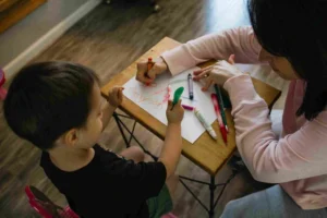 Boy Writing on a Paper with a Woman Assisting Him - Why Preschool Teachers Are Important 