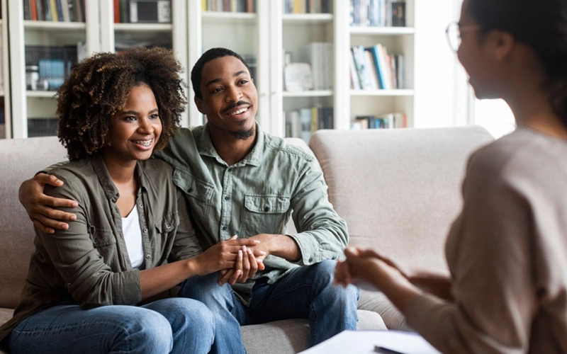 A couple holding hands and smiling during a therapy session, showcasing a supportive and comforting counseling environment.