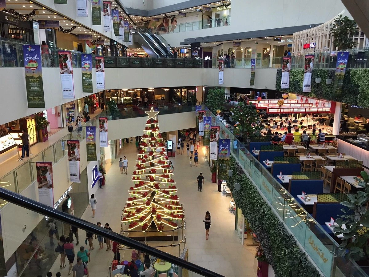 Busy indoor shopping mall with Christmas decorations, featuring a large tree, food courts, and retail stores.