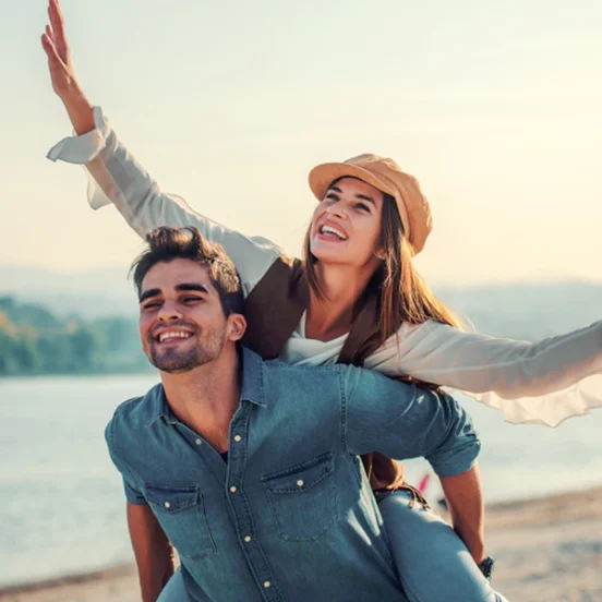 Understanding Complacency in Relationships. Joyful couple by the lake, with the woman playfully riding on the man's back, enjoying a carefree moment together.