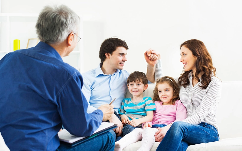 A family of four sitting on a couch, engaged in a conversation with a therapist, highlighting a family therapy session aimed at improving communication and relationships.